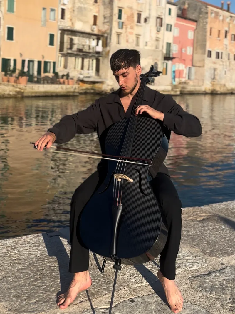 Vito spielt Cello auf einer Hafenmauer bei Sonnenuntergang